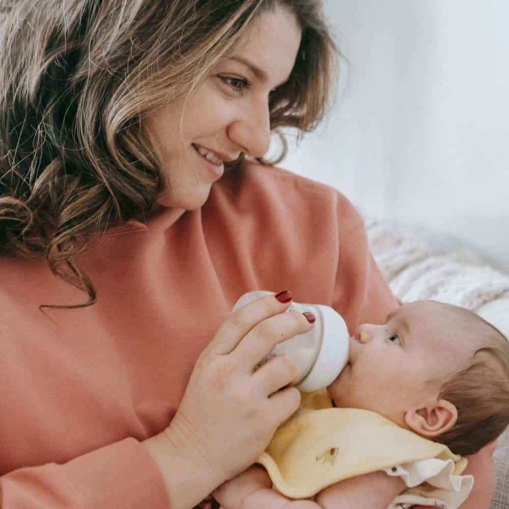 Mère redressée donnant le biberon, le bébé à hauteur de poitrine