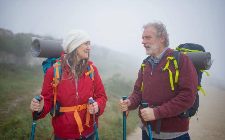 Pareja de más de 60 años caminando por un sendero de montaña con bastones