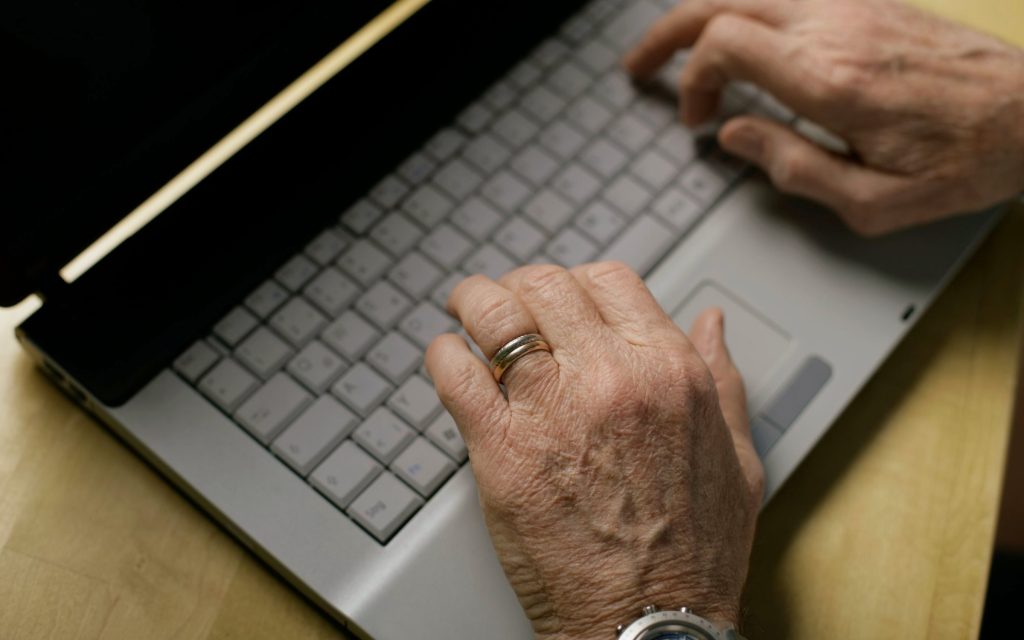 Manos de una persona mayor escribiendo en el teclado de un portátil