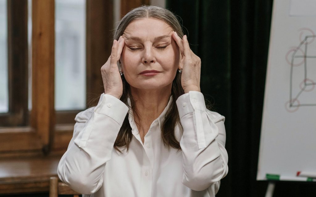 Mujer de unos 50 años frente al ordenador, con los dedos en las sienes y los ojos cerrados