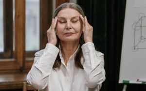 Mujer de unos 50 años frente al ordenador, con los dedos en las sienes y los ojos cerrados